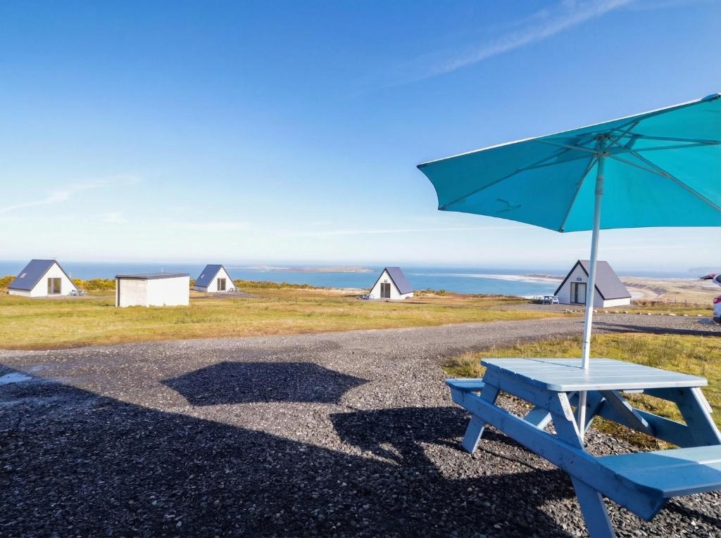 a blue bench with an umbrella and some houses at Cabin 8 Inis Dumhaigh in Gortahork