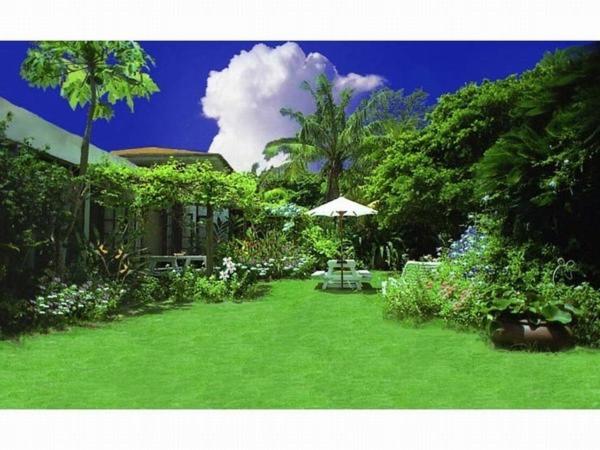 a green yard with an umbrella and a house at Pension Iriomote in Iriomote