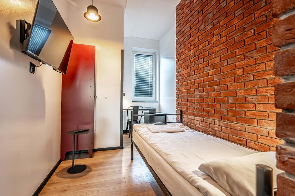 a brick wall in a room with a bed and a tv at Vola Hostel in Warsaw