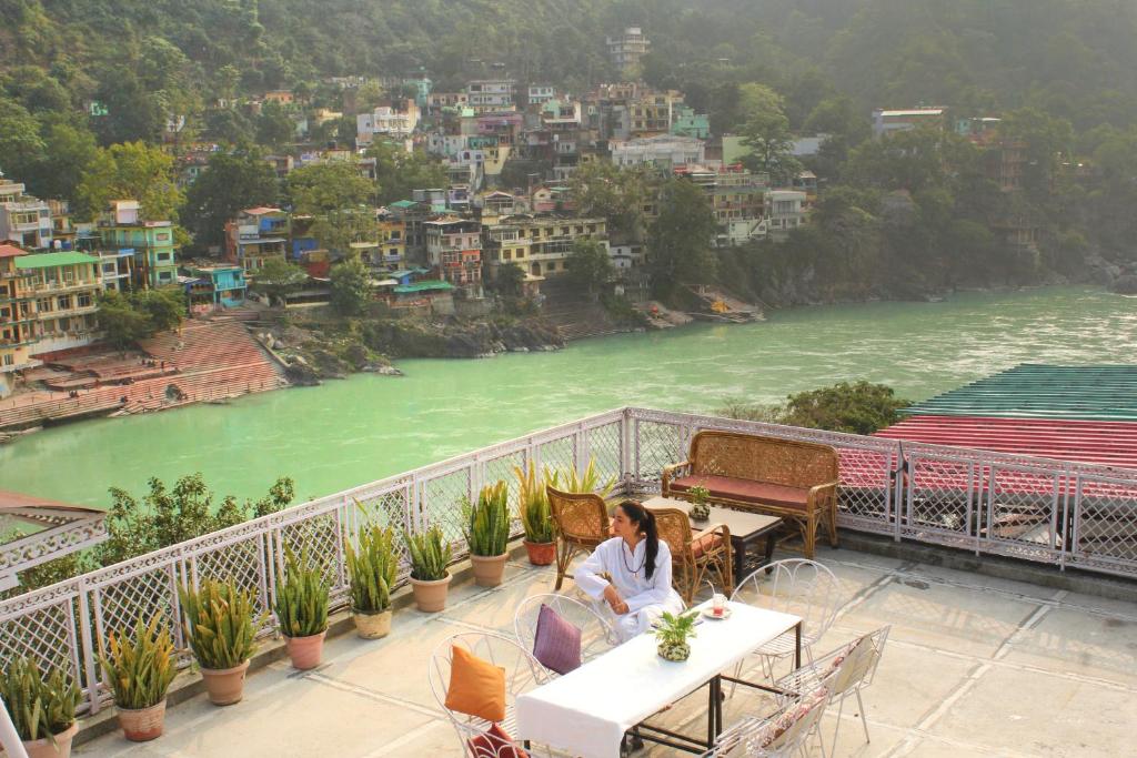 a woman sitting at a table on a balcony overlooking a river at Hotel Ishan - A Ganges Riverside Retreat by Salvus in Rishīkesh