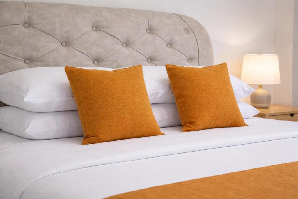 a white bed with two orange pillows on it at Heidi's Guesthouse in Siquijor