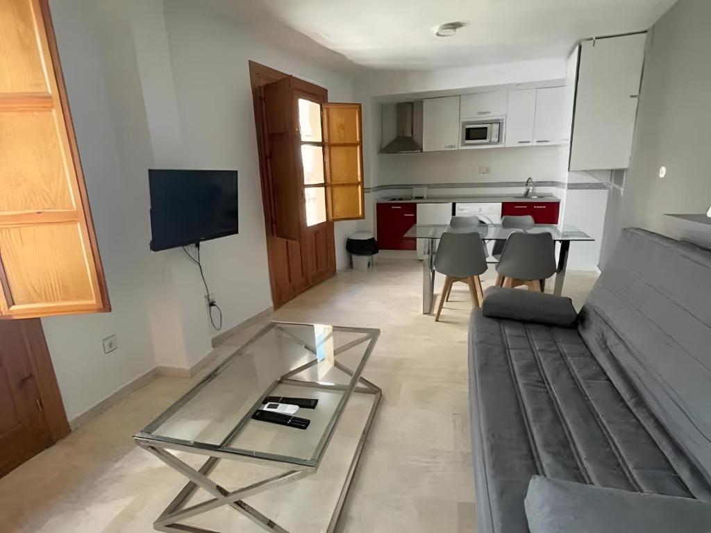 a living room with a glass table and a kitchen at Apartamentos Silleria - A 4 min de la Catedral de Granada in Granada