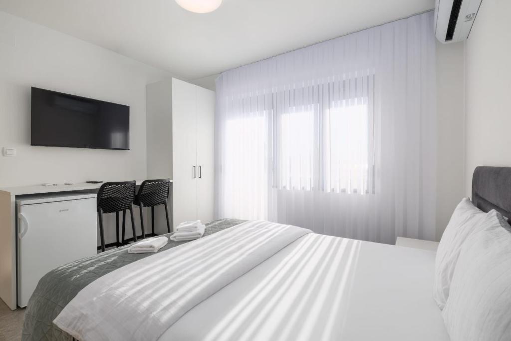 a white bedroom with a large bed and a tv at Apartments Rea in Krk