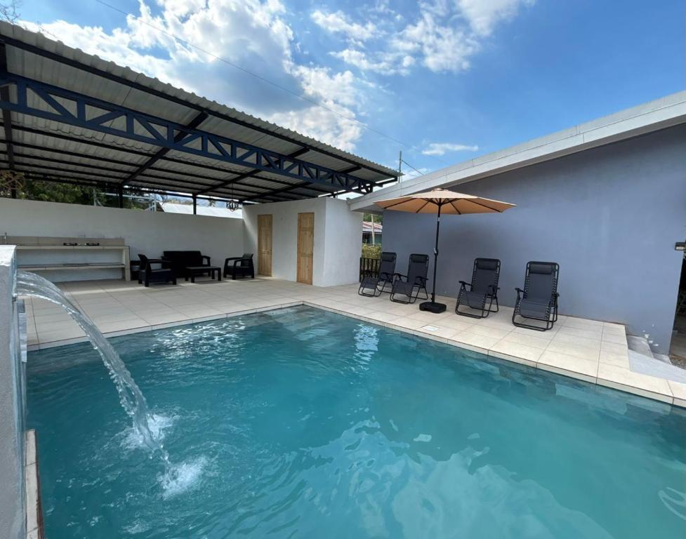 a swimming pool with a patio with chairs and an umbrella at Casa Celeste Río Grande in Paquera
