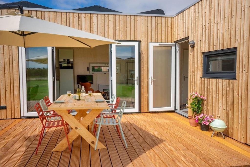a wooden deck with a table and an umbrella at De Lepelaar - Ecohuisjes Terschelling in Midsland