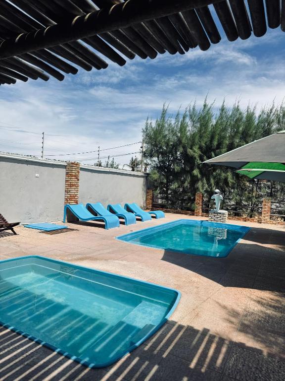 a swimming pool with blue chairs and an umbrella at Pousada e Chalés mar e sol in Manibu