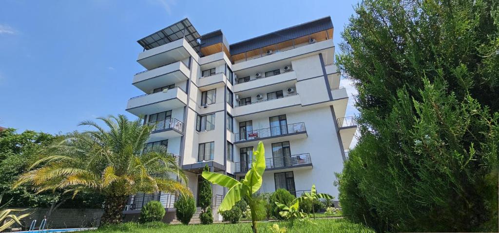 a white building with a palm tree in front of it at Riva in Kobuleti