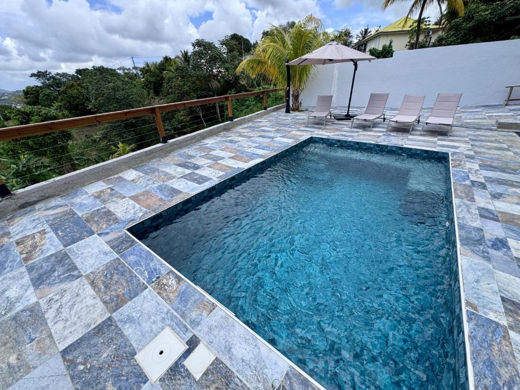 a swimming pool with chairs and an umbrella at Appartement Mango in Rivière-Salée