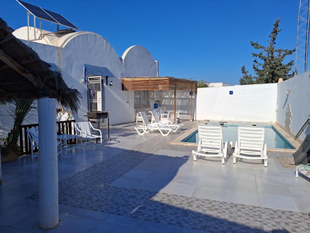 a patio with white chairs and a swimming pool at Maison Amina Villa Novel in Triffa