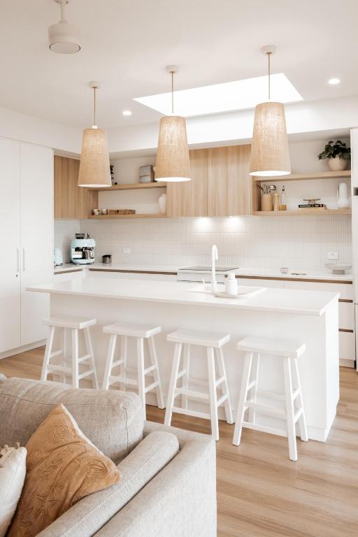 a kitchen and living room with a white island and stools at Bay Days - Binalong Bay in Binalong Bay