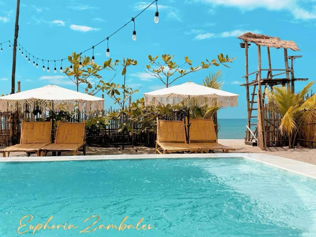 a swimming pool with chairs and umbrellas next to the beach at Euphoria Zambales in Botolan