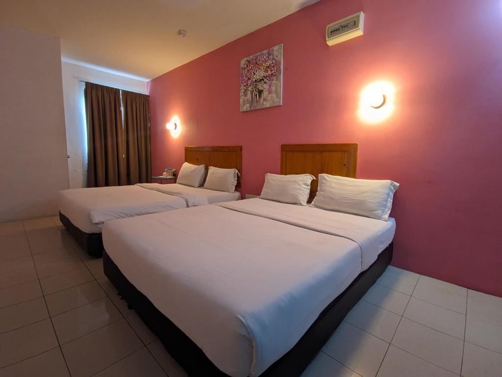 two beds in a room with a red wall at Midah Inn Puchong in Puchong