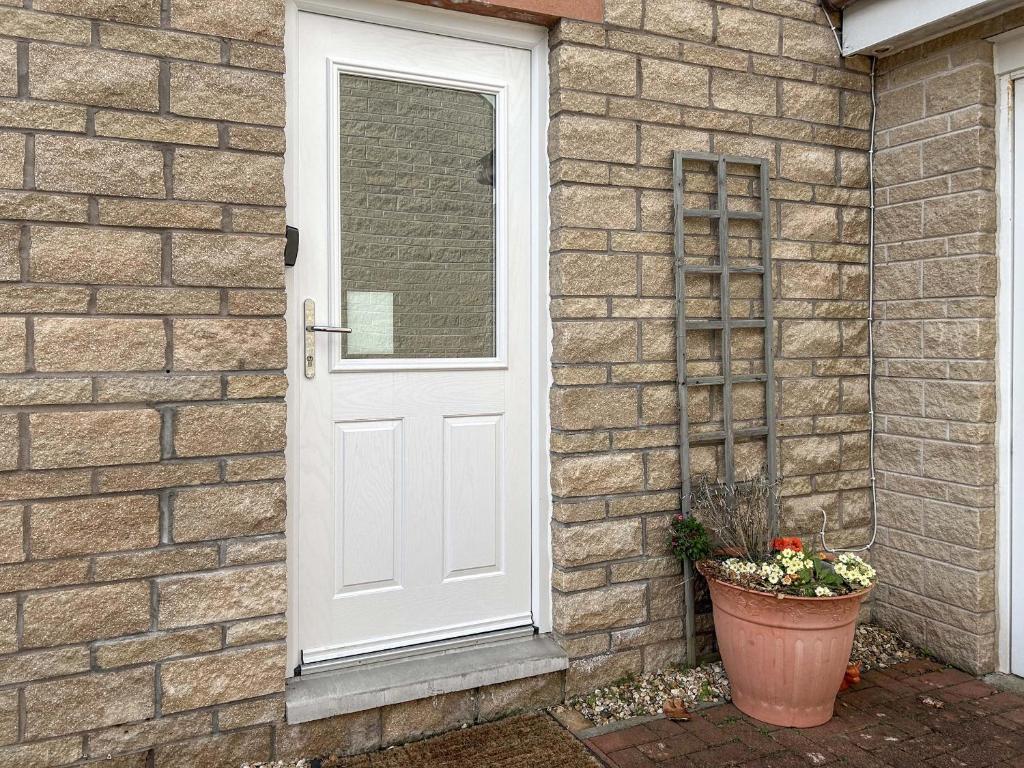 a white door on a brick house with a flower pot at Peebles Apartment in Peebles