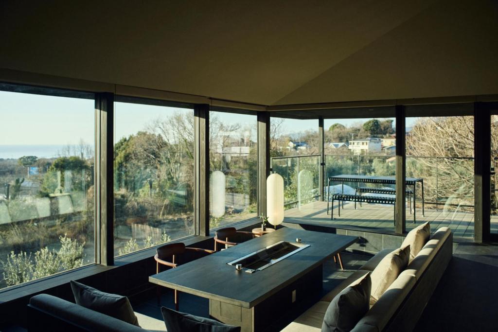 a dining room with a table and chairs and large windows at Hiire IZU OLIVE in Ito