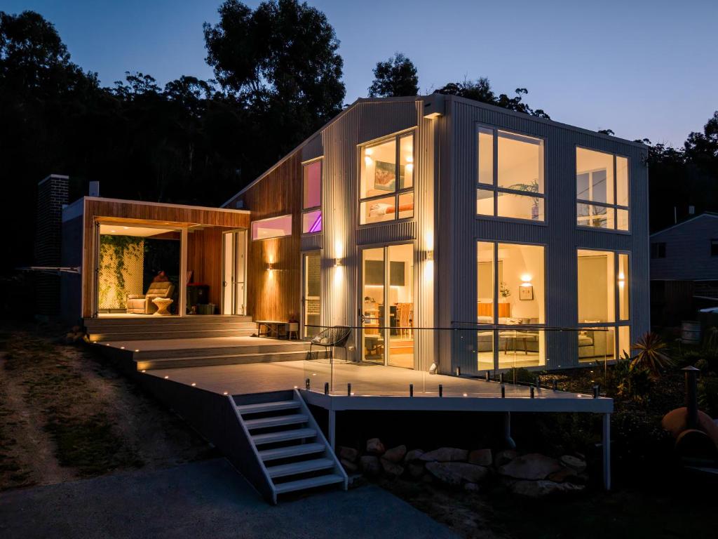 a large glass house with a staircase in front of it at Tasman Tides - Architecturally-designed holiday home in Eaglehawk Neck