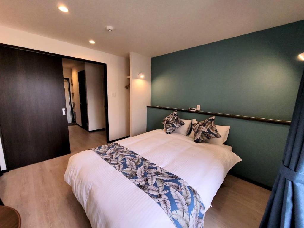 a bedroom with a large white bed with a green wall at PRIME TREE Izumizaki CONDO HOTEL in Naha