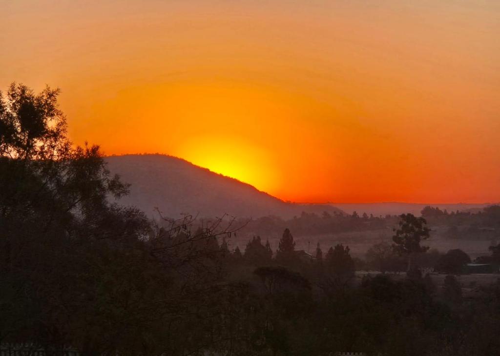 a sunset over a hill with the sun setting at Hornbill Self Catering Cottages Muldersdrift in Krugersdorp