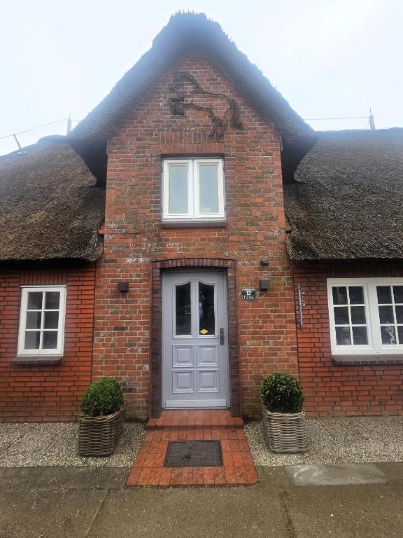 a brick house with a grey door and two windows at Uijs Hüs in Borgsum