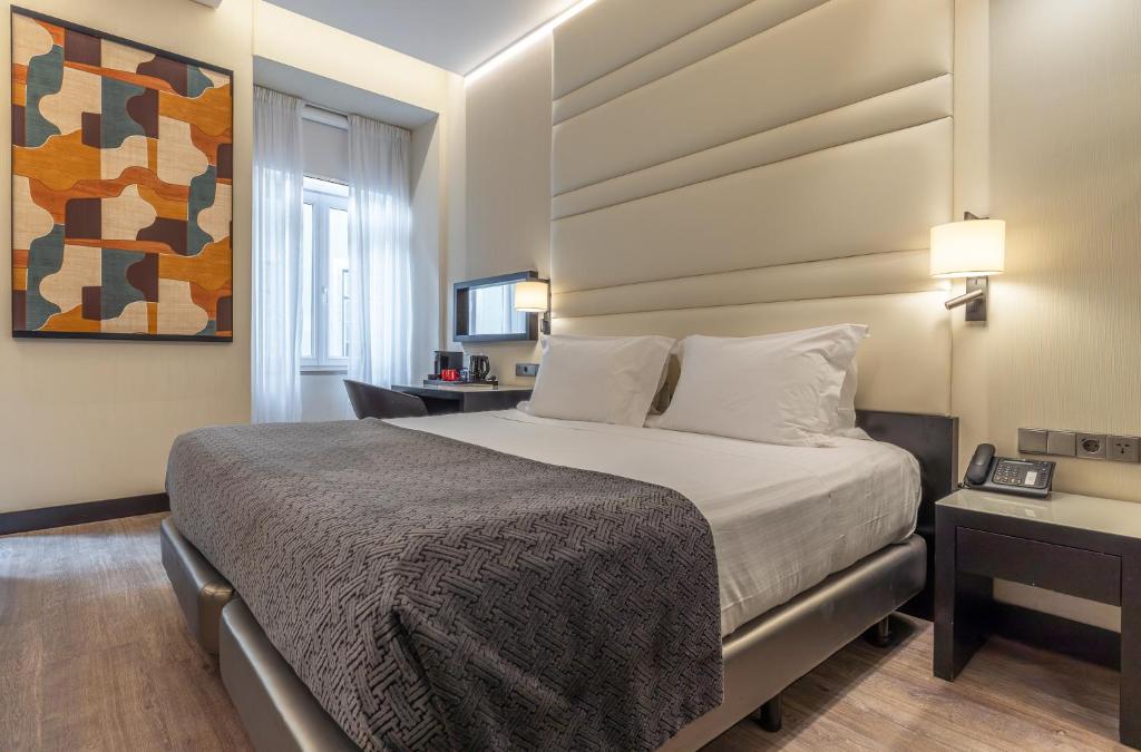 A large double bed anchors a bright room with a desk, artwork and window.