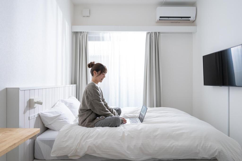 a woman sitting on a bed with a laptop at stella stay in Imari