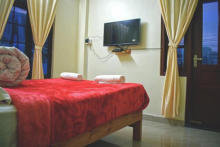 a room with a bed with a red blanket and a tv at Mebaker View Inn in Shillong