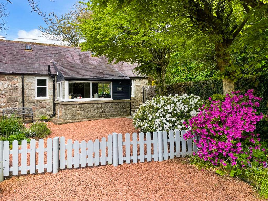 a white picket fence in front of a house with flowers at Craigrannoch Cottage in Rockcliffe