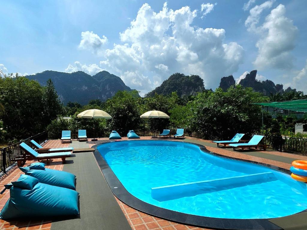 a swimming pool with chairs and mountains in the background at Khaosok Impress in Khao Sok National Park