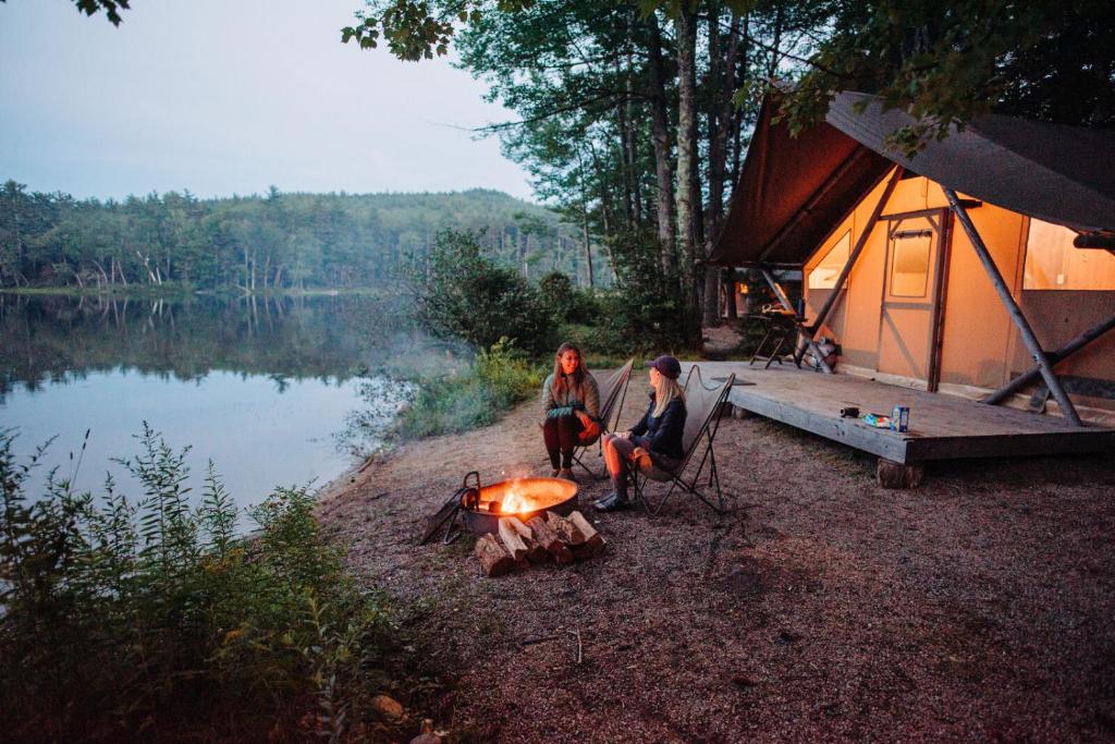 two women sitting around a fire in front of a tent at Huttopia White Mountains in Albany