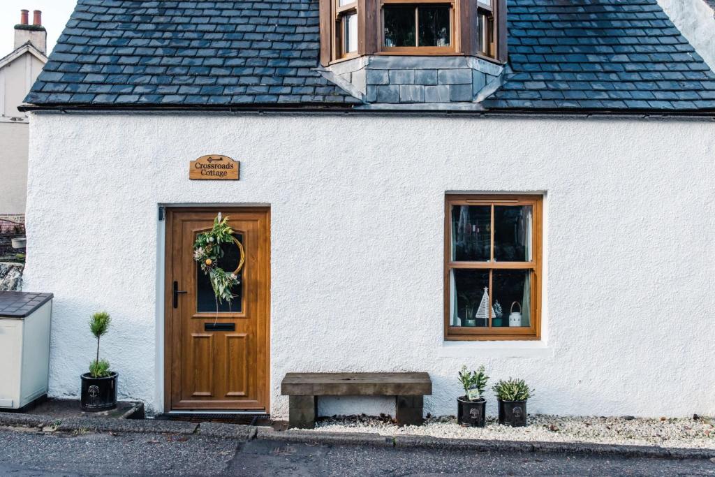 a white building with a wooden door and a bench at Crossroads Cottage in Drumnadrochit