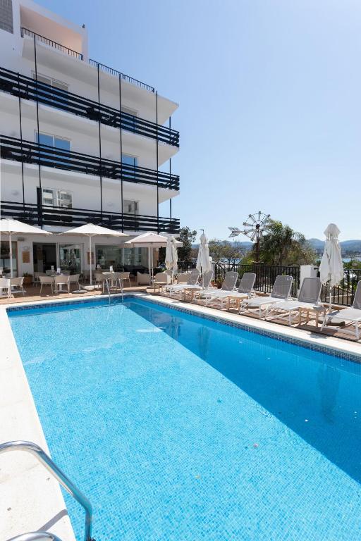 a large swimming pool with chairs and a building at Es Mitjorn Hotel in San Antonio