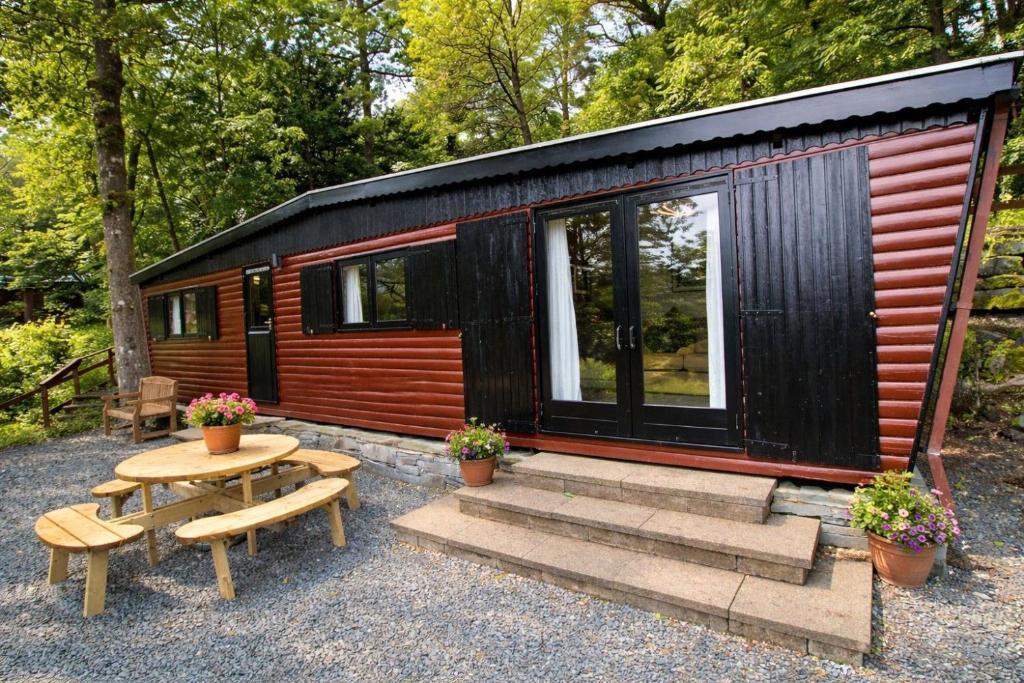 a small cabin with a picnic table and benches at Neaum Crag Lodge ideal for a couple or family with young children in a woodland setting at Skelwith Bridge in Grasmere