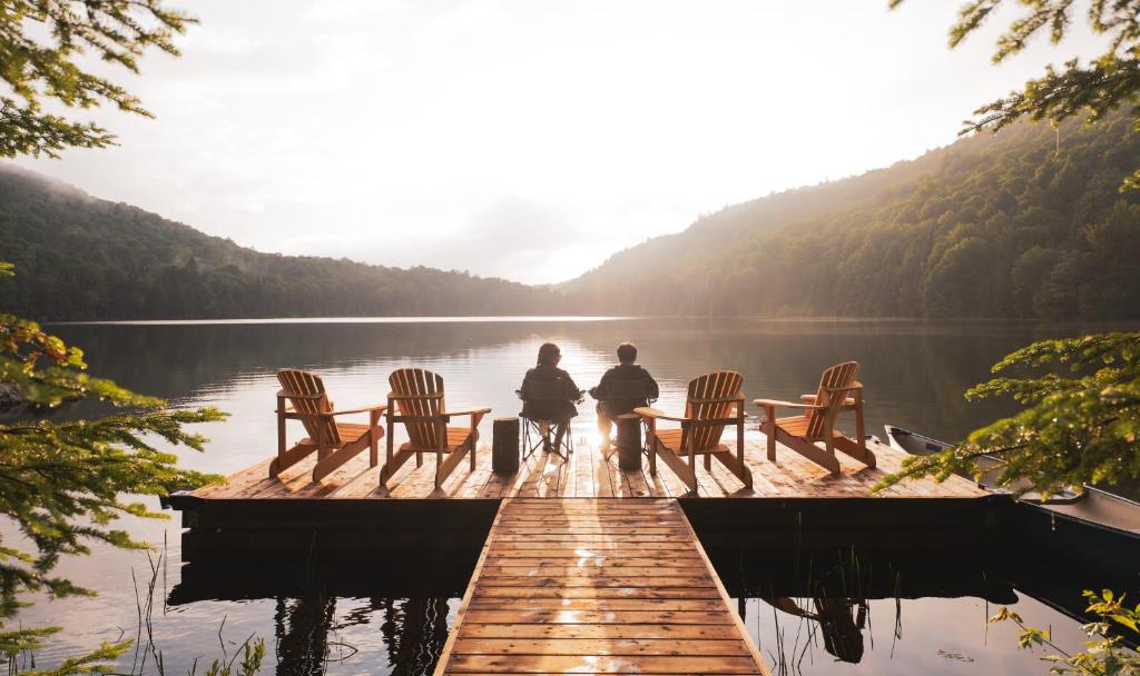 two people sitting on a dock on a lake at Huttopia Les Deux Lacs - Laurentides in Saint-Faustin