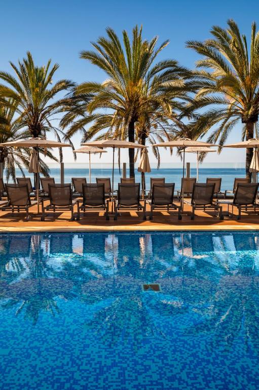 a swimming pool with chairs and palm trees and the ocean at Hapimag Apartments Marbella in Marbella