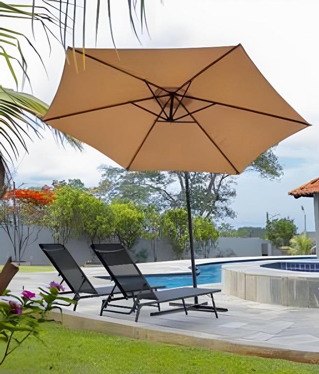a large umbrella over two chairs and a pool at Studio Hebron: Refúgio Entre a Cidade e a Natureza in Anápolis