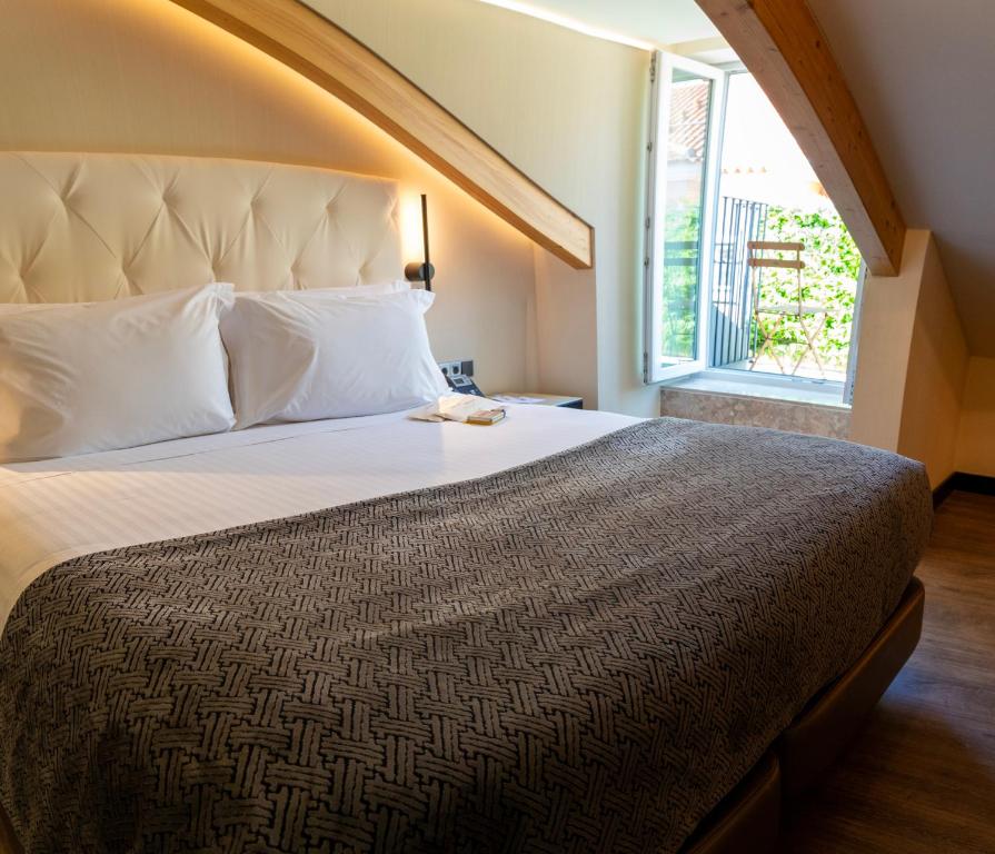 A large bed in an attic-style room with an open window and exposed timber beams.