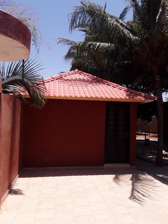 a red building with a red roof and palm trees at Chambre simple à louer in Fatick