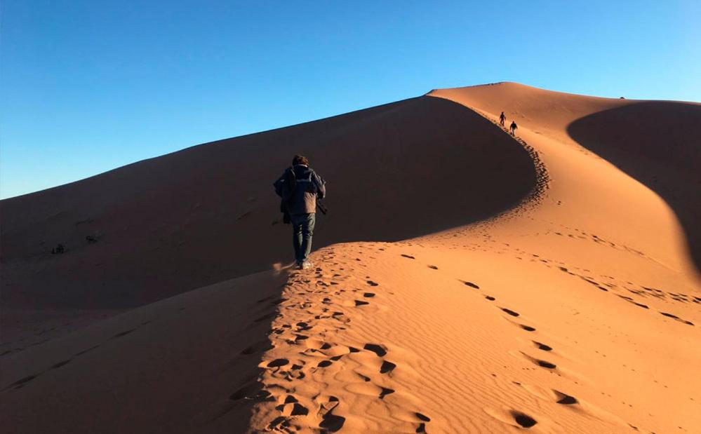 a man walking on a sand dune in the desert at Dunes Activity Camp in Mhamid