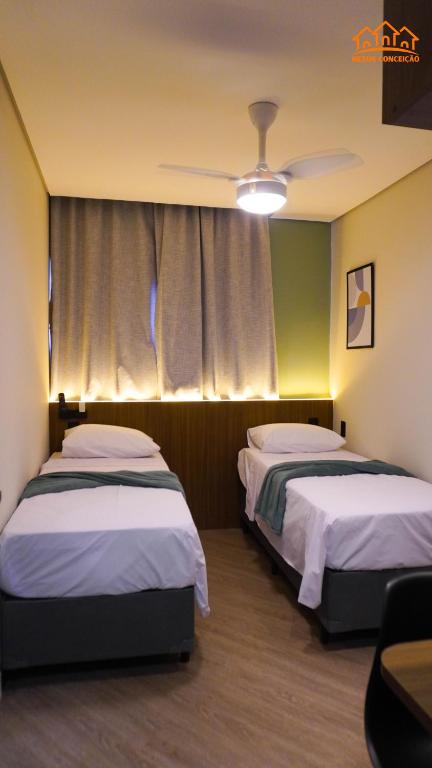 two beds in a hotel room with a ceiling fan at Nexus Conceição in São Paulo