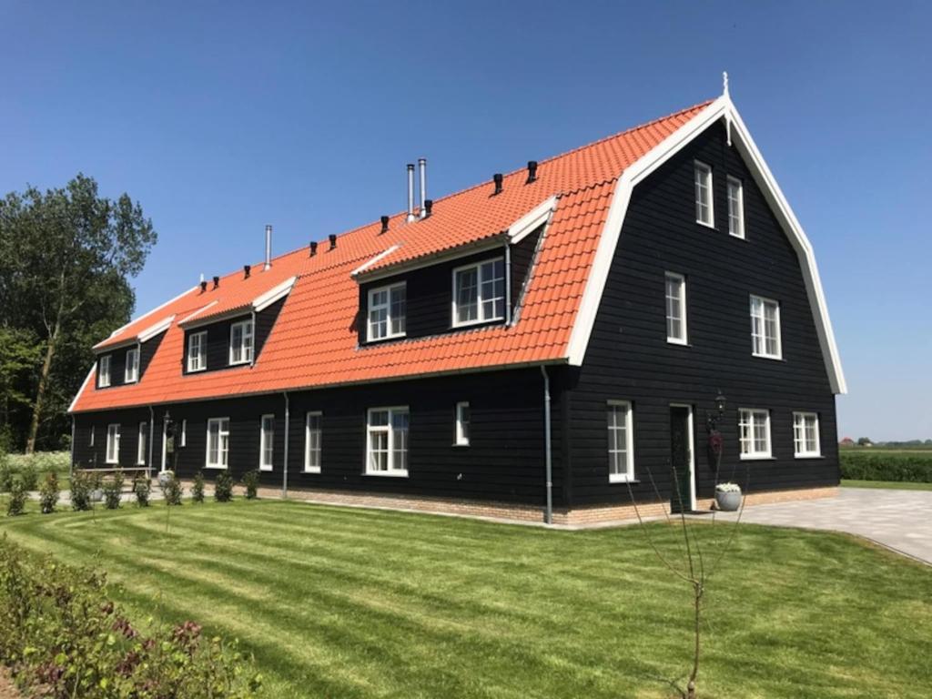 a large black barn with an orange roof at Grand Villa with Sauna & Jacuzzi in Den Burg