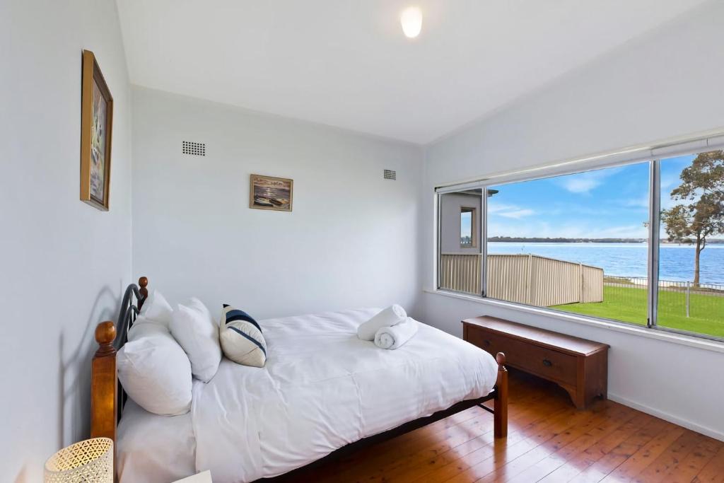 a bedroom with a bed and a large window at Lakes Edge Cottage Pet Friendly Waterfront Escape in Budgewoi