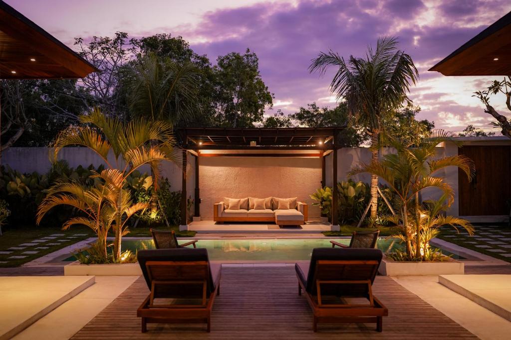 a patio with a couch and a pool with palm trees at The Placo Villa Uluwatu in Denpasar
