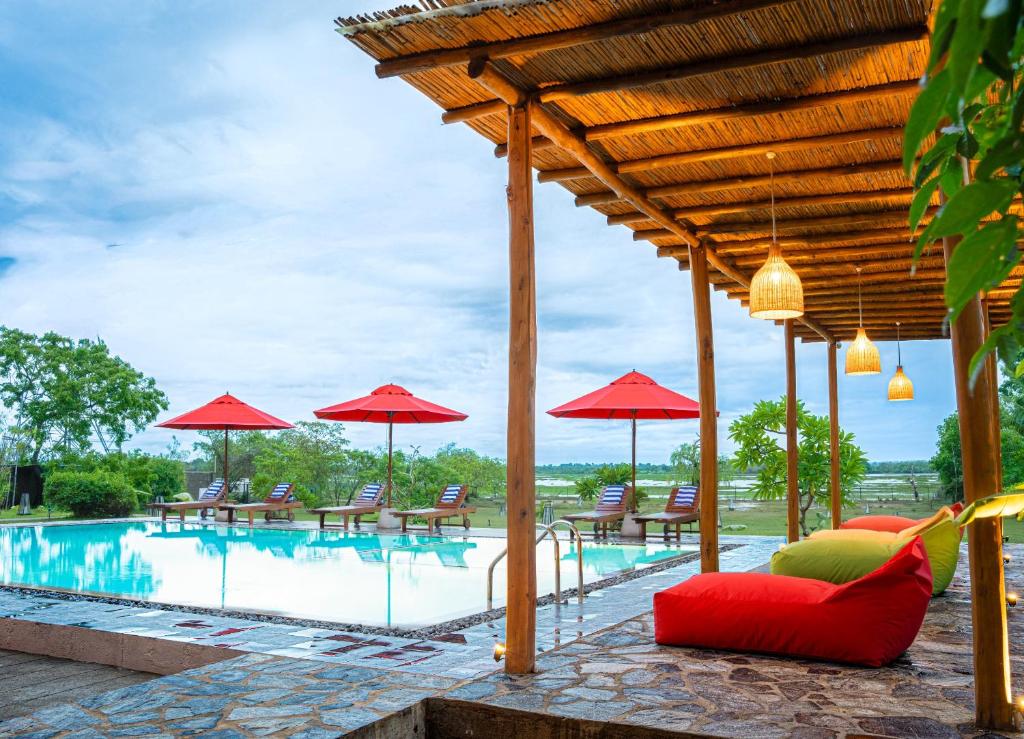 a pool with red umbrellas and tables and chairs at Chaarya Lake in Tissamaharama