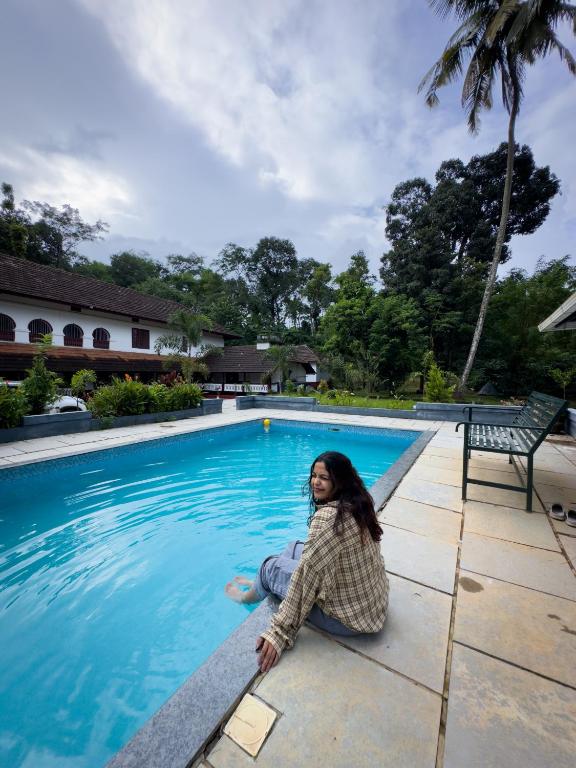 a woman sitting next to a swimming pool at Keloth Tharavadu in Panamaram