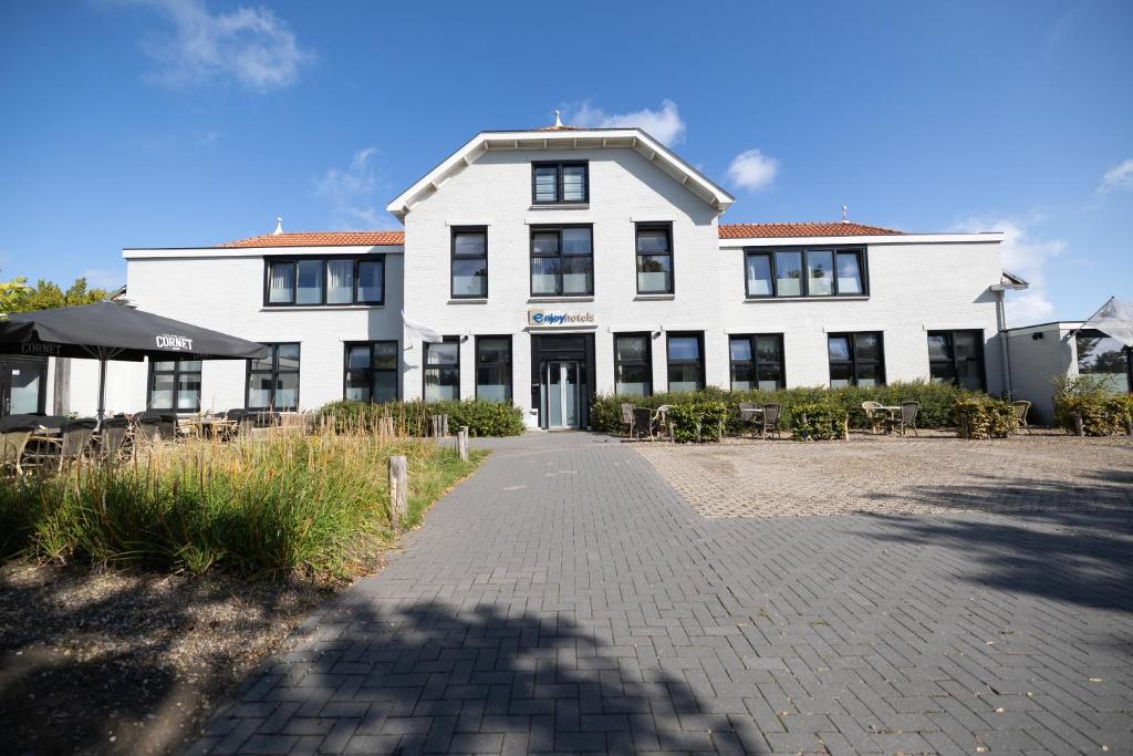 a white building with tables and chairs in front of it at Strandhotel Wemeldinge in Wemeldinge