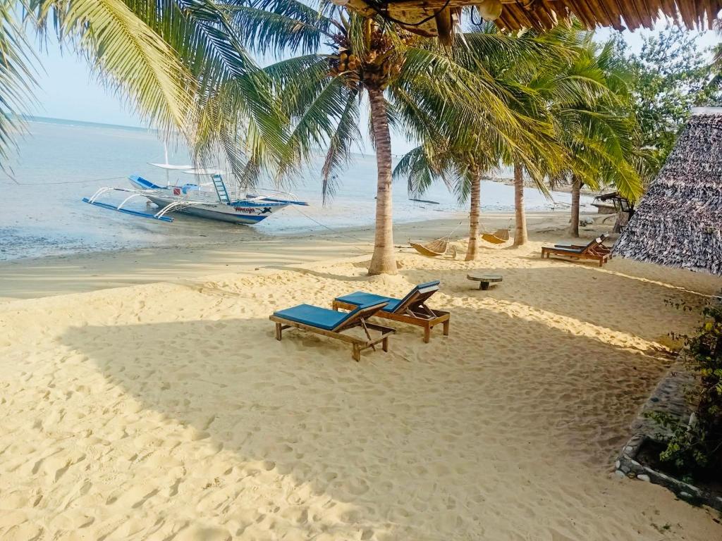 a beach with chairs and palm trees and a boat at Mecaja Beach House in Roxas