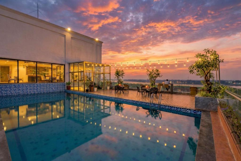 a swimming pool in front of a building with a sunset at Aaron Riverview Hotel in Vientiane