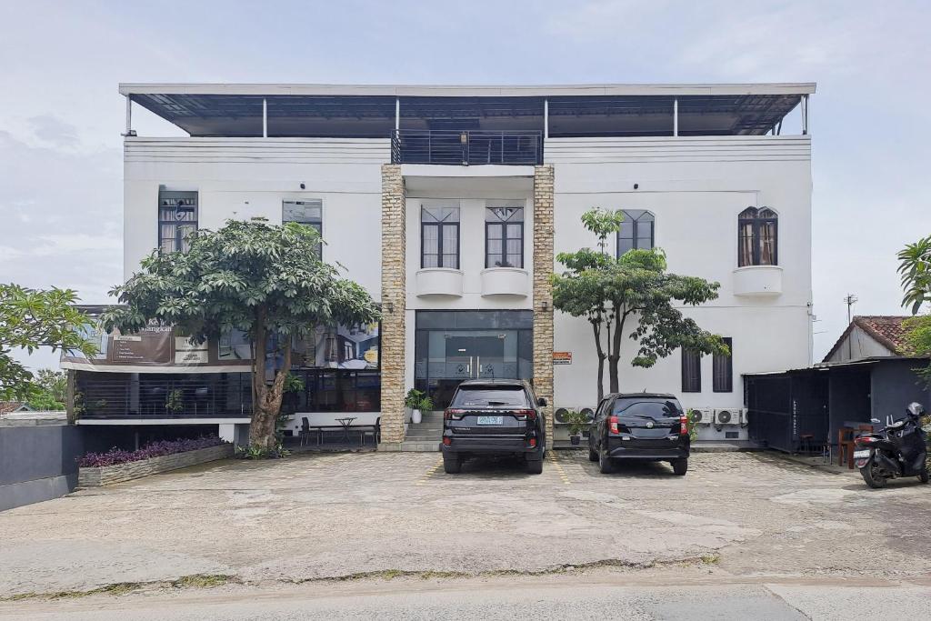 two cars parked in front of a white building at SANS Stay Raja Soeta Hostel Lampung in Hajimana