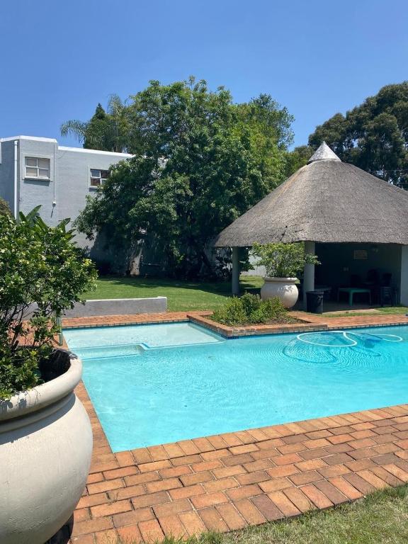 a swimming pool with a grass umbrella and a table at Villa Elizabeth - Fourways Gardens Sandton in Fourways