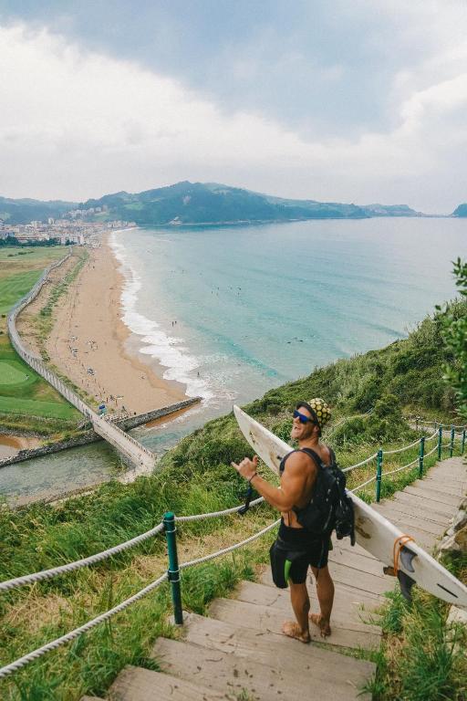 a man walking up a hill with a surfboard at San Sebastian Surf and Party Hostel in Aia
