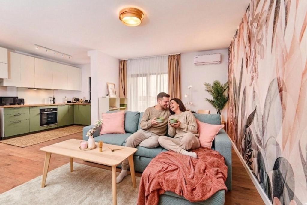 a man and woman sitting on a couch in a living room at Matcha Garden apartment in Dumbrăviţa